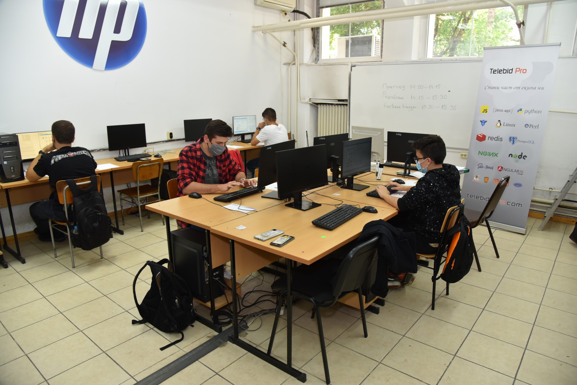 Изпитна зала с брандинг на HP и Telebid Pro и разписание на изпита на бяла дъска на Националното състезание по компютърни мрежи 2021 г.